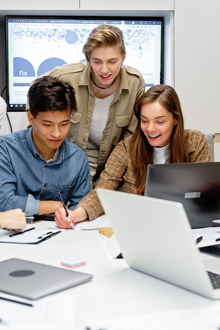 Three colleagues collaborating on a project with laptops in a modern office setting.